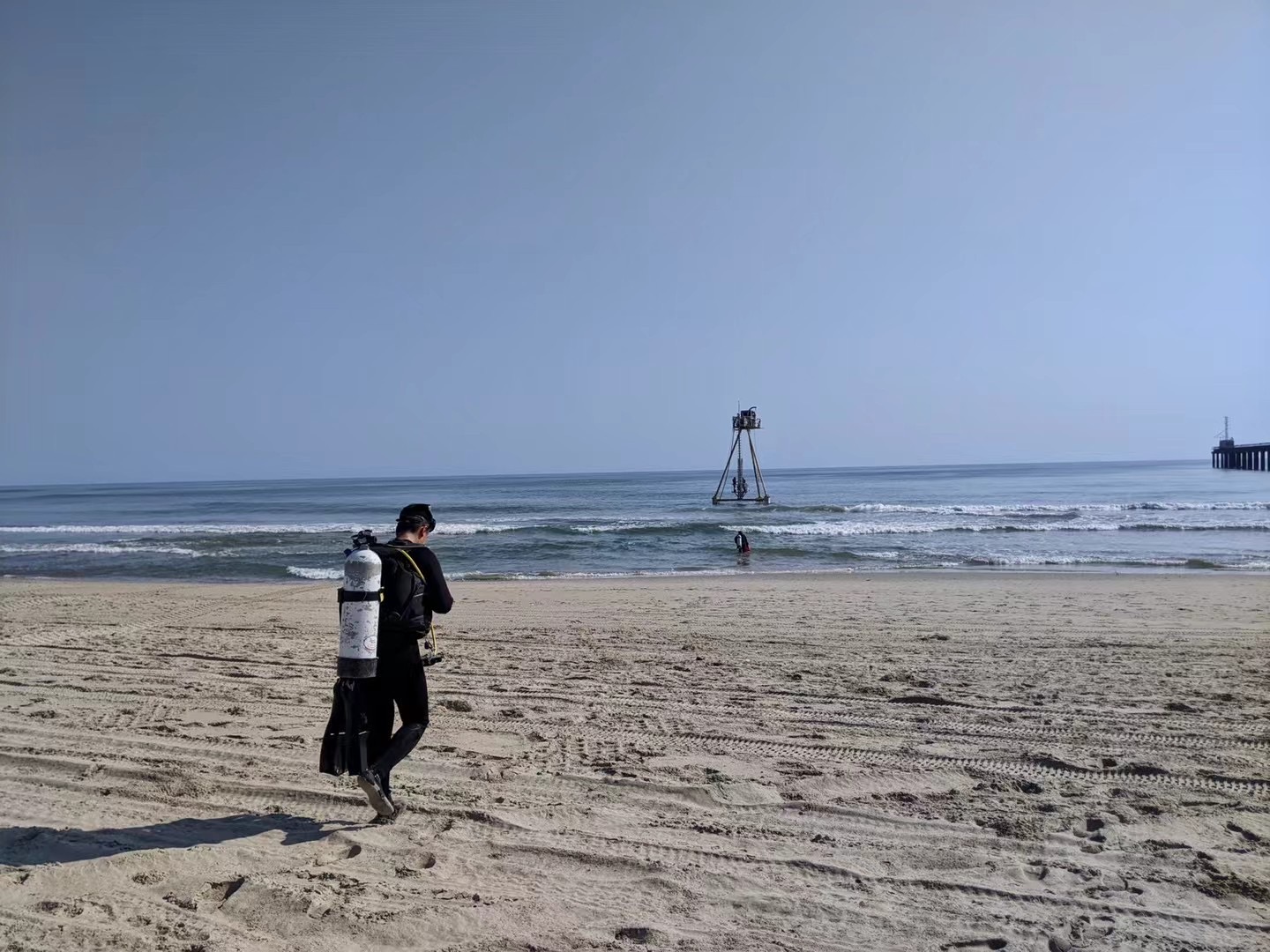 A diver entering a beach field site with an offshore instrument tower